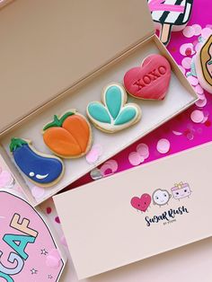 some decorated cookies are in a box on a pink table with confetti and candies