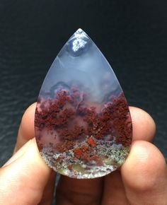 a hand holding a piece of glass with red dirt inside