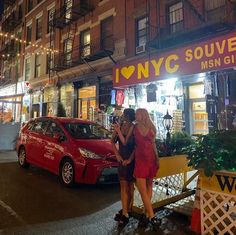 two women are standing in front of a store at night, one is holding her hand on the other's shoulder