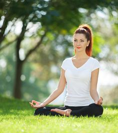 a woman is sitting in the grass and meditating with her eyes closed while doing yoga