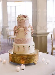 a three tiered wedding cake with pink flowers on top and candles around the base