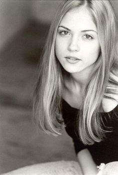 black and white photograph of a woman with long blonde hair sitting on a couch looking at the camera