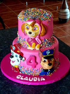 a pink birthday cake with paw patrol characters on the top and sprinkles