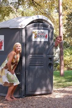 a woman in a dress standing next to a portable toilet on the side of a road