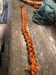 an orange rope on top of a wooden table next to some balls of string and yarn