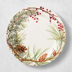 a white plate with pine cones and berries on the rim is sitting on a marble surface