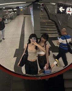 two women are standing on the escalator looking at their cell phones and taking pictures