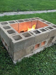 a fire pit made out of cinder blocks in the grass with flames coming from it