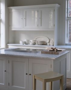 a kitchen with white cabinets and marble counter tops in front of a large open window