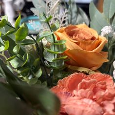 an assortment of flowers are arranged on a table with greenery and other things in the background