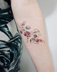 a woman's arm with berries and leaves tattoo on the left side of her arm