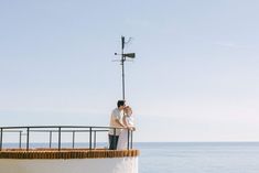 a man and woman standing next to each other on top of a roof near the ocean