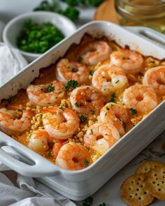 a casserole dish filled with shrimp and garnished with parsley next to crackers