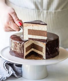 a woman is cutting into a chocolate cake on a white platter with two slices taken out