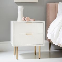 a white nightstand next to a bed in a room with gray walls and pink headboard