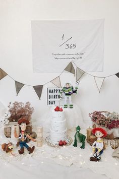 a birthday cake surrounded by figurines and bunting on a table in front of a banner