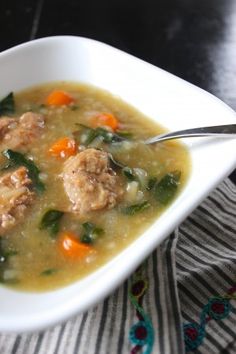 a bowl of soup with meatballs and carrots on the side next to a spoon