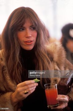 a woman in fur coat holding a drink and looking at her cell phone stock photo