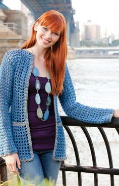 a woman with red hair is leaning on a fence near the water and smiling at the camera