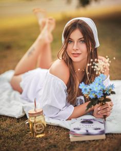 a beautiful young woman laying on top of a blanket next to a bouquet of flowers