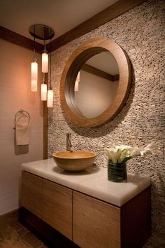 a bathroom sink under a round mirror next to a vase with flowers