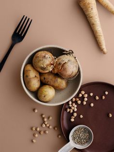 a bowl filled with potatoes next to some garlic and other vegetables on a plate, along with a fork