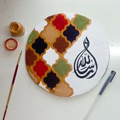 a plate with an arabic calligraphy on it next to paintbrushes and paints