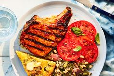 a white plate topped with meat, tomatoes and beans next to a glass of water