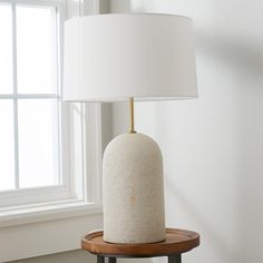 a white lamp sitting on top of a wooden table next to a window in a room