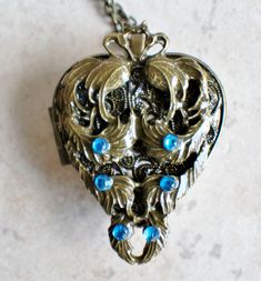 an ornate heart shaped locke with blue stones on a silver chain hanging from a marble surface