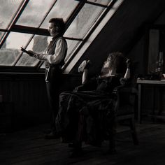 a man and woman sitting in chairs looking out the window at something on the ground