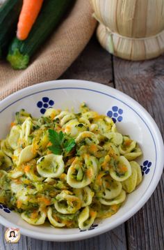 a white bowl filled with pasta and vegetables on top of a wooden table next to carrots