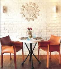 two chairs sitting at a table in front of a white brick wall with a sun shaped mirror above it