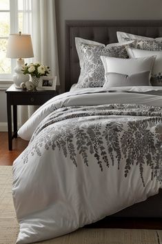 a bed with white and grey comforters in a bedroom next to a window,