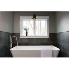 a white bath tub sitting under a window next to a vase with flowers on it