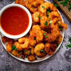 a white plate topped with fried shrimp next to a bowl of tomato sauce and parsley