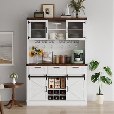 a white cabinet with wine glasses and other items on the top shelf next to a potted plant