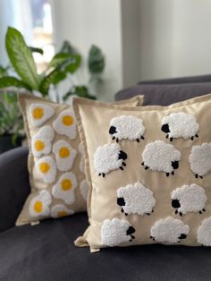 two pillows with black and white sheep on them sitting on a couch next to a potted plant