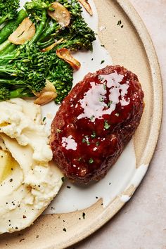 a white plate topped with meat, mashed potatoes and broccoli covered in ketchup