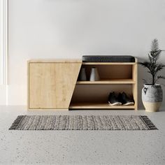 a wooden cabinet with shoes on it next to a potted plant in a white room