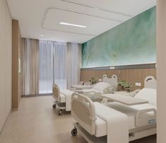 an empty hospital room with white beds and green painting on the wall behind glass doors