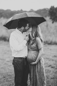 a pregnant couple kissing under an umbrella in the rain