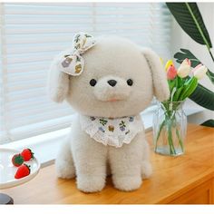 a white stuffed dog sitting on top of a table next to a vase with flowers