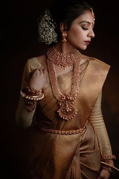 a woman in a brown sari with gold jewelry on her neck and hands behind her back