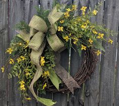 a wreath with yellow flowers and greenery on a wooden fence next to a wire fence