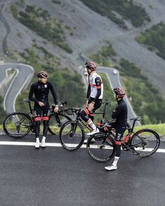 three men are standing next to their bikes on the road in front of a mountain