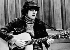 black and white photograph of a man playing an acoustic guitar in front of a microphone