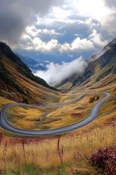 a winding road in the middle of a mountain range with clouds rolling over it's sides