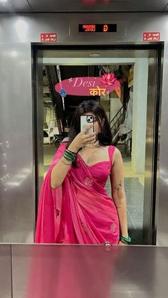 a woman in a pink sari taking a selfie with her cell phone while standing on an escalator