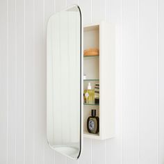 a bathroom mirror and shelf with bottles on the wall next to each other in a white room